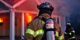 Bombero con equipo de respiración autónomo frente a una casa en llamas.
