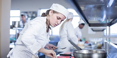 Una persona con gorro de chef cocinando en una cocina.
