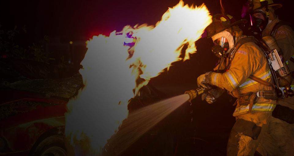 A firefighter spraying water on a burning car