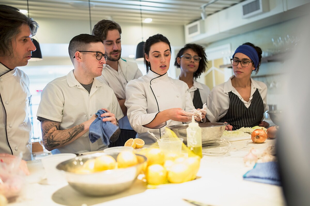 Una cocinera experta explicando una receta a los demás cocineros.
