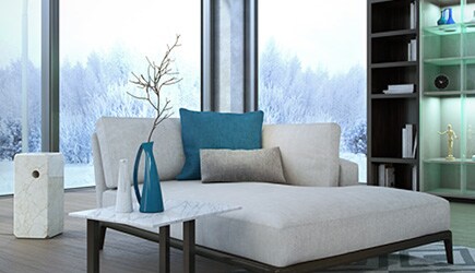 A chaise lounge creates a cozy nook in front of floor-to-ceiling windows that overlook snow-covered trees.