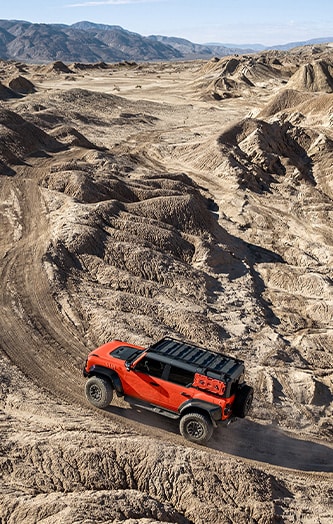 Todoterreno con vinilo decorativo rojo habanero circulando por un terreno escarpado en el desierto con montañas en el horizonte.
