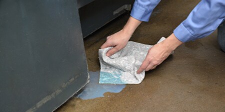 Persona utilizando el kit antiderrame de 3M para absorber un líquido derramado en el suelo.
