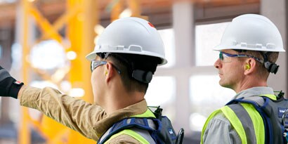 backview of two workers wearing hardhats and pointing at something
