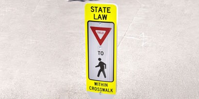 Sign with letters and symbols reading “State law: Yield to pedestrians in crosswalk.”
