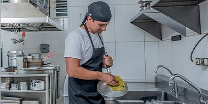 Un trabajador de cocina comercial frota una sartén en un fregadero.
