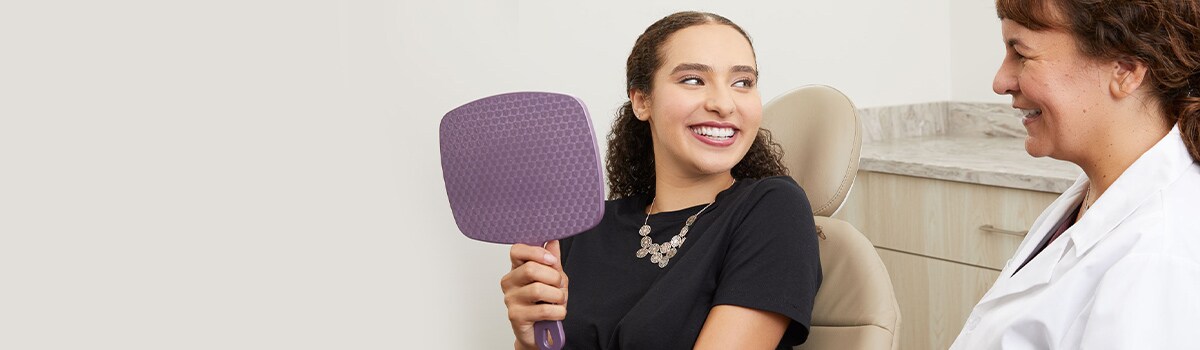Orthodontist with patient smiling holding mirror
