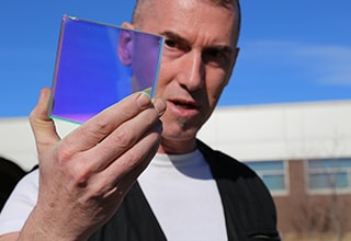 Artist, Philip Blackburn, holds up a piece of 3M Dichroic Film, a material he used in building a 22-foot kaleidoscope.
