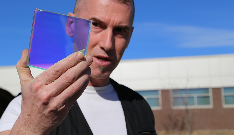 Artist, Philip Blackburn, holds up a piece of 3M Dichroic Film, a material he used in building a 22-foot kaleidoscope.