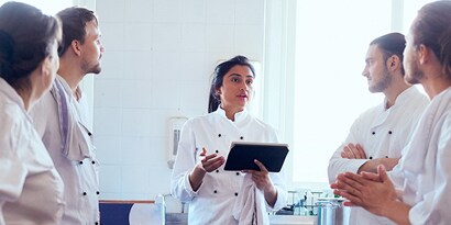 Cinco empleados discutiendo, uno sostiene un tablet en la mano.
