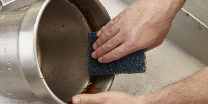 Un primer plano de una persona lavando un cuenco con la fibra de uso rudo de 3M.