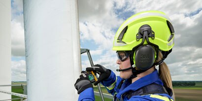 sideview of woman on wind tower wearing climbing helmet and earmuffs
