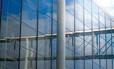 Edificio con grandes ventanales que reflejan el cielo y las nubes.
