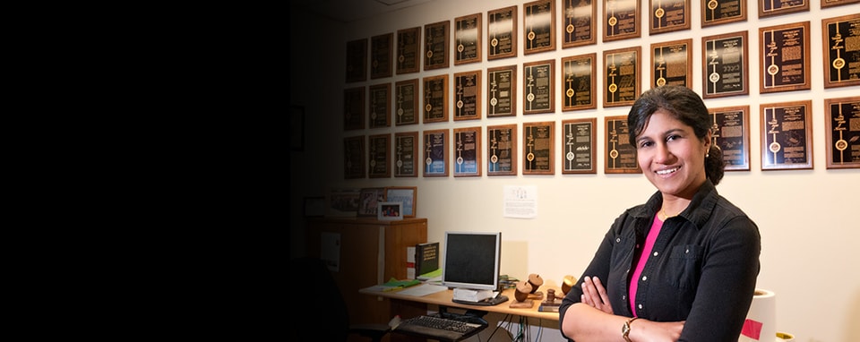 3M Corporate scientist, Jayshree Seth standing before plaques awarded to her for each of her patents.