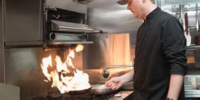 Un chef cocinando con una sartén al fuego.
