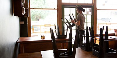 Un empleado de restaurante apilando bancos encima de una mesa vacía.
