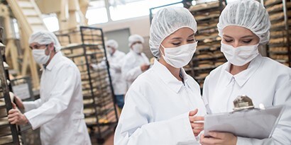 Trabajadores usando mascarillas y gorros confieren en una cocina comercial.
