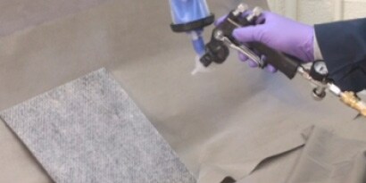 Liquid adhesive being sprayed onto fabric using applicator
