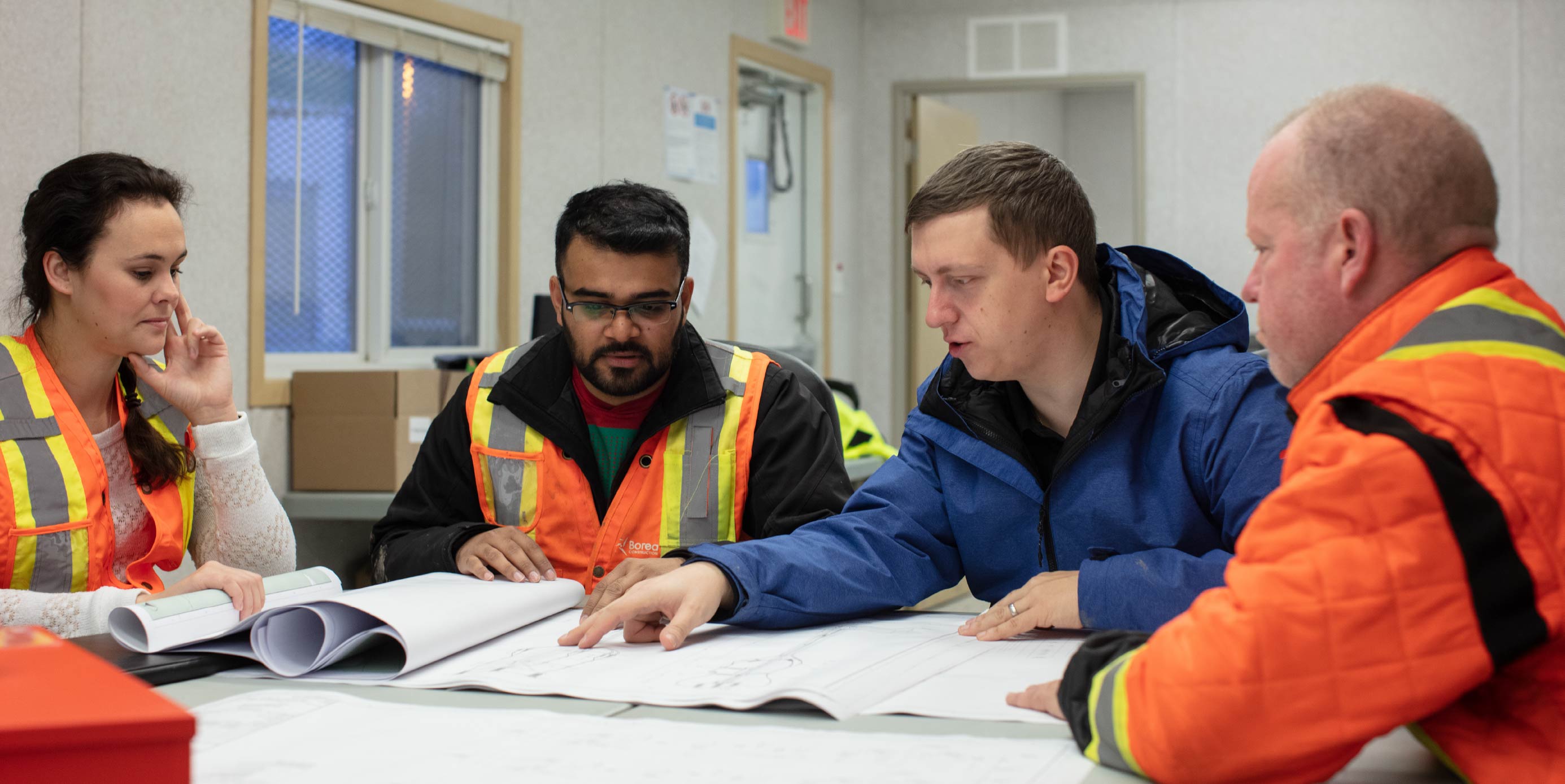 Equipo de construcción analiza planos en una mesa dentro de oficina de obra.
