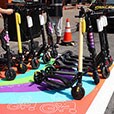 Colorful painted pavement for scooter parking on urban road, with scooters and person holding handlebars of scooter.