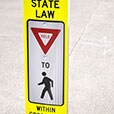 Sign with letters and symbols reading “State law: Yield to pedestrians in crosswalk.”