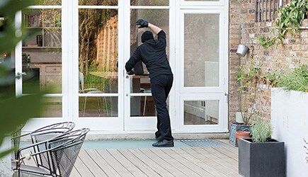 A person dressed in all black tries to look into a home he might want to rob through a window with reflective, security-enhancing window films.