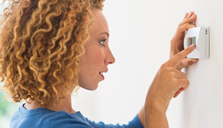 A young woman adjusts the temperature on her thermostat.