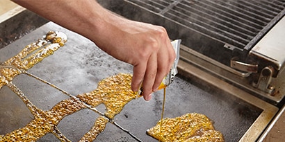 Una persona vertiendo el Líquido de Limpieza Rápida para Planchas 3M™ Scotch-Brite™ sobre una plancha caliente.
