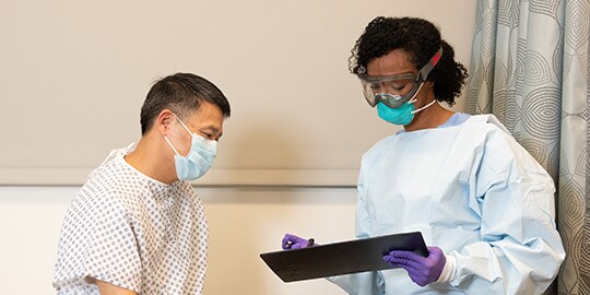 Clinician wearing PPE speaking with a patient
